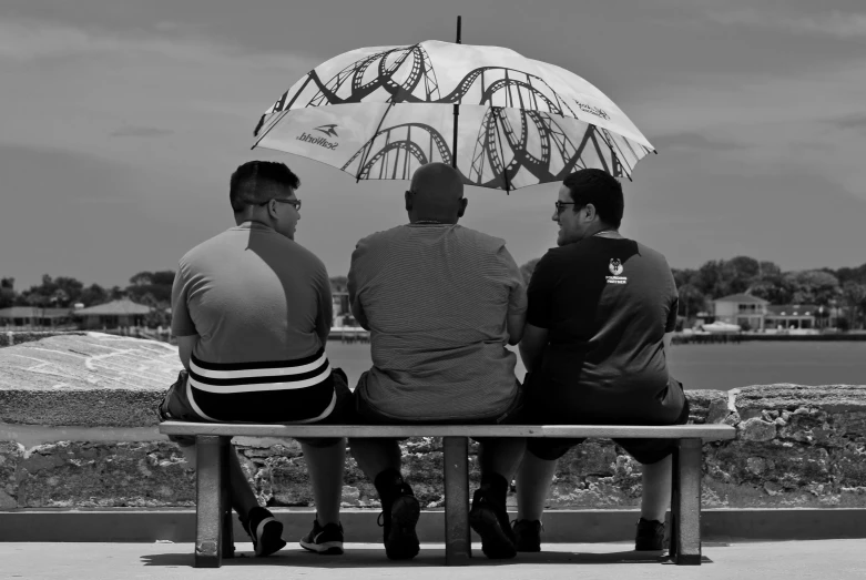 three men sitting on a bench near the water