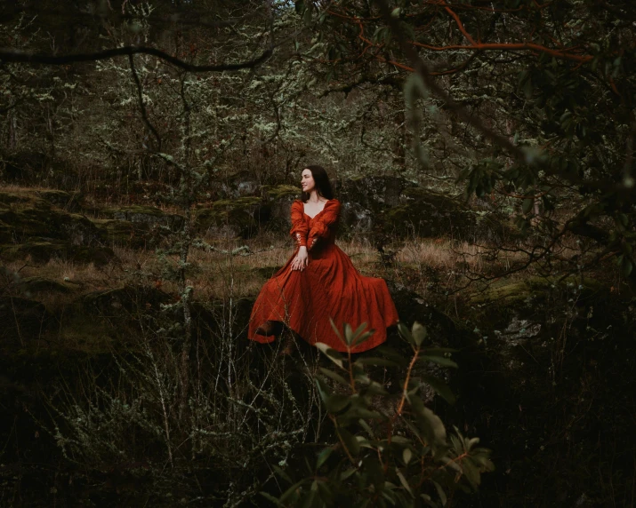 a woman in a long red dress sitting on a nch