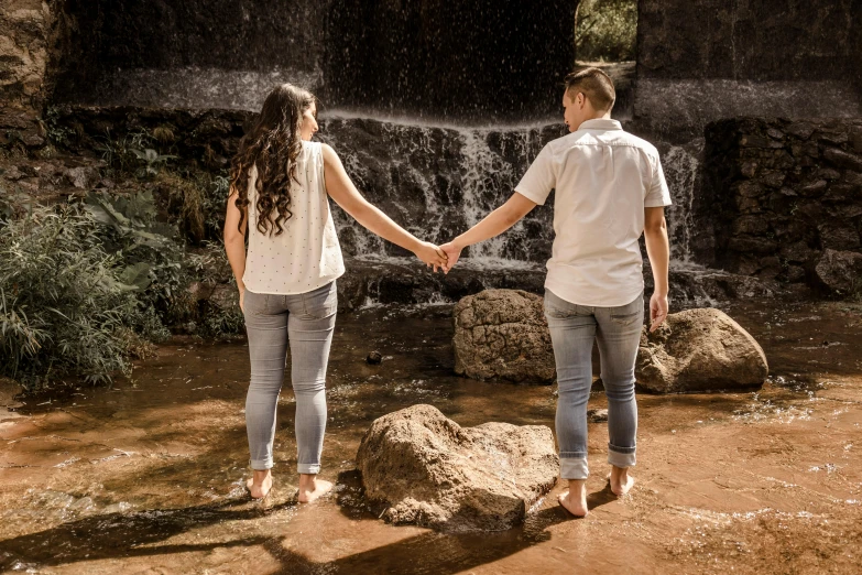 a man and woman hold hands next to a waterfall