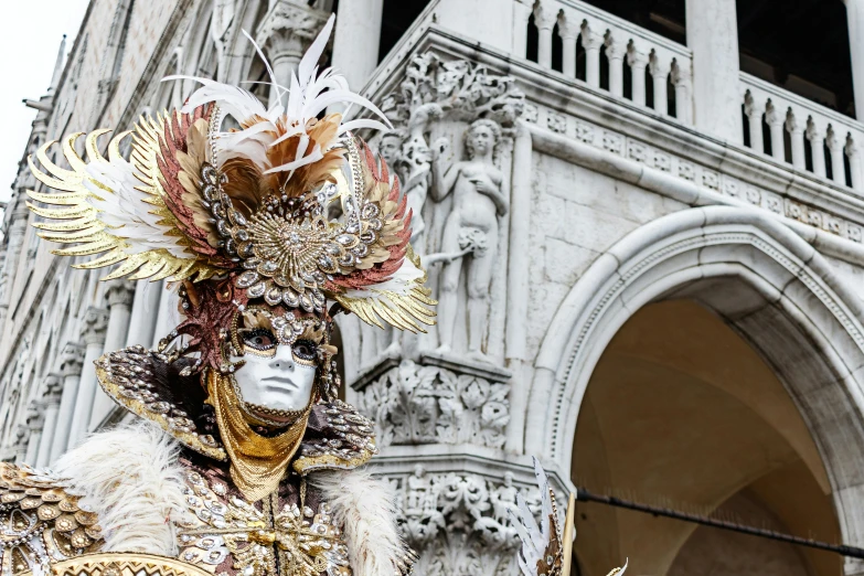 a large statue wearing a feather and feather mask in front of a tall white building