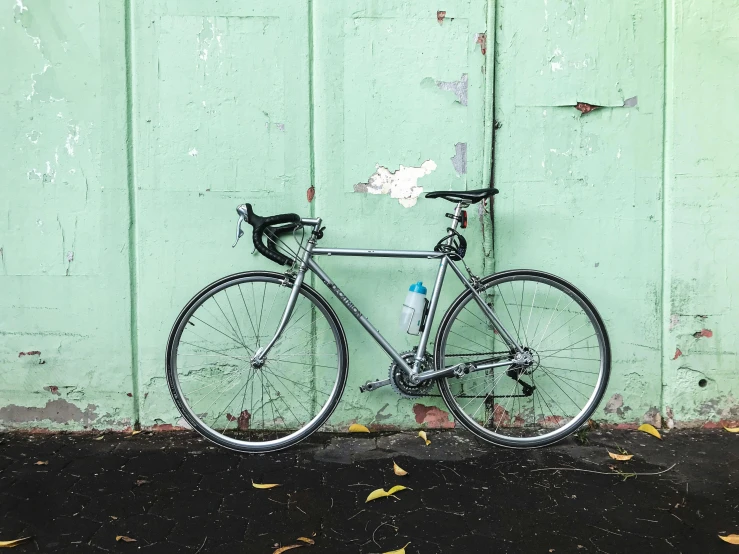 a bicycle leaning against the green wall on top of asphalt