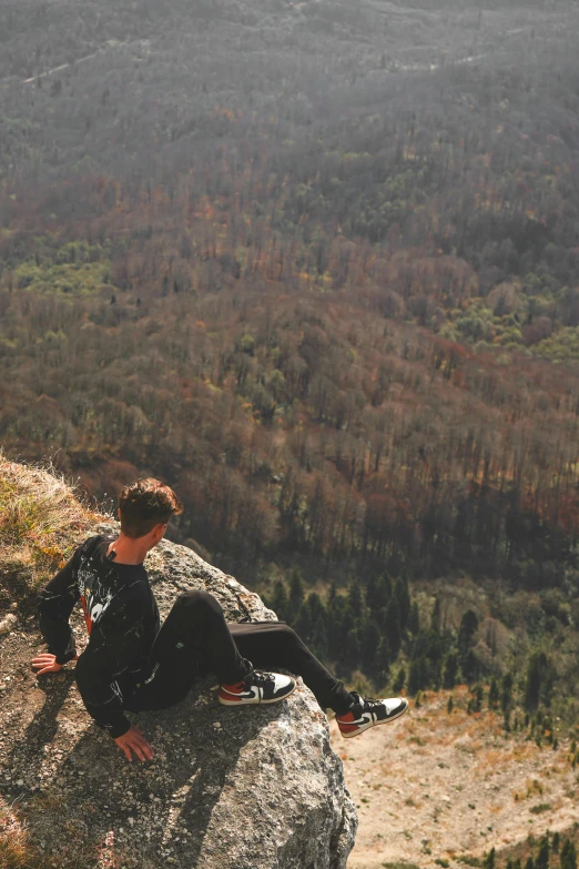 a young man sitting on a rock by himself