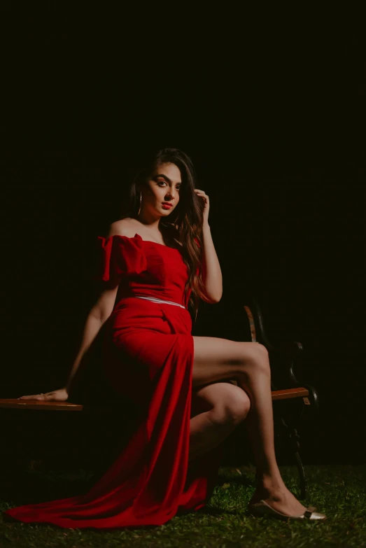 a beautiful woman in a long red dress sitting on a bench