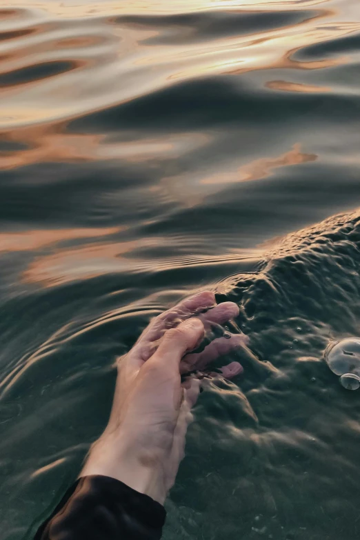 a person's hand reaching for soing above the water