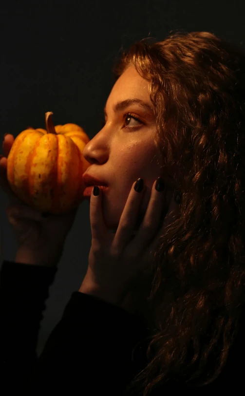 a woman holding an orange while standing next to a pumpkin