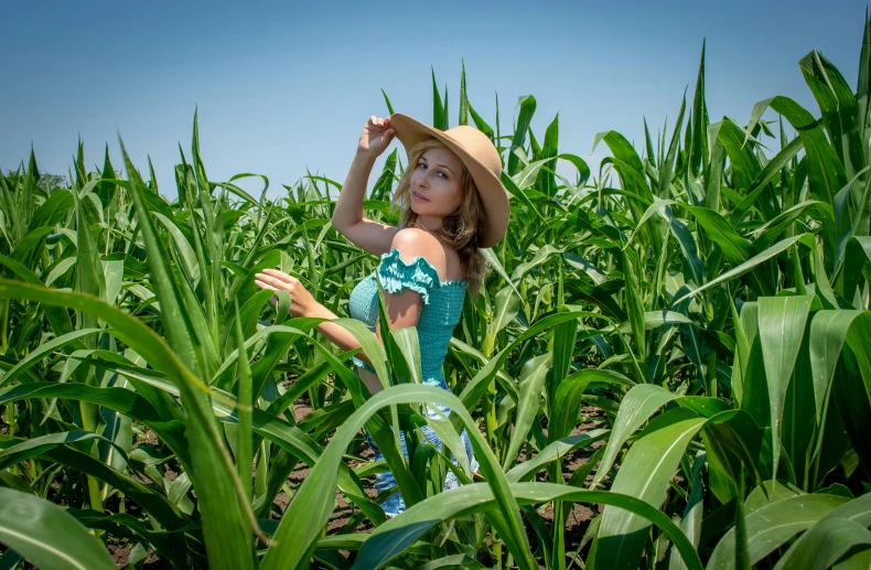 a girl wearing a dress and hat standing in the middle of a field