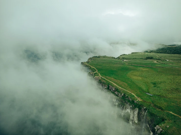 a cliff surrounded by green fields and clouds