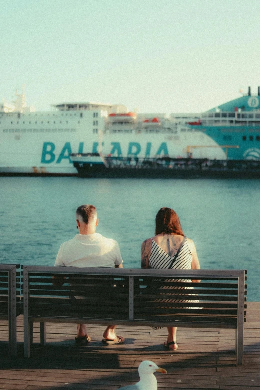 a couple sits on a bench next to the sea