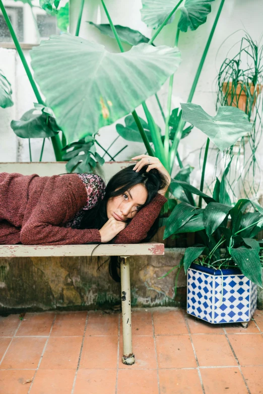 a woman laying on top of a bench near plants