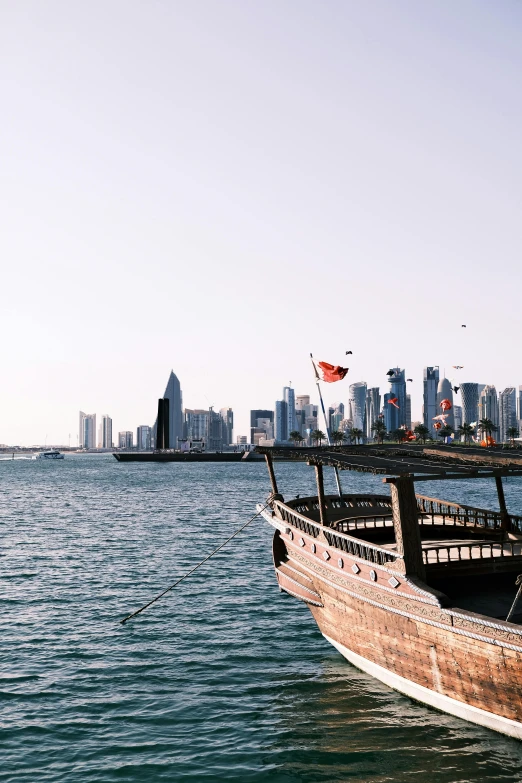 an old boat sitting on the water in front of a city skyline