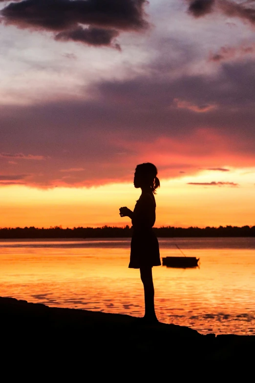 a girl standing on the beach at sunset