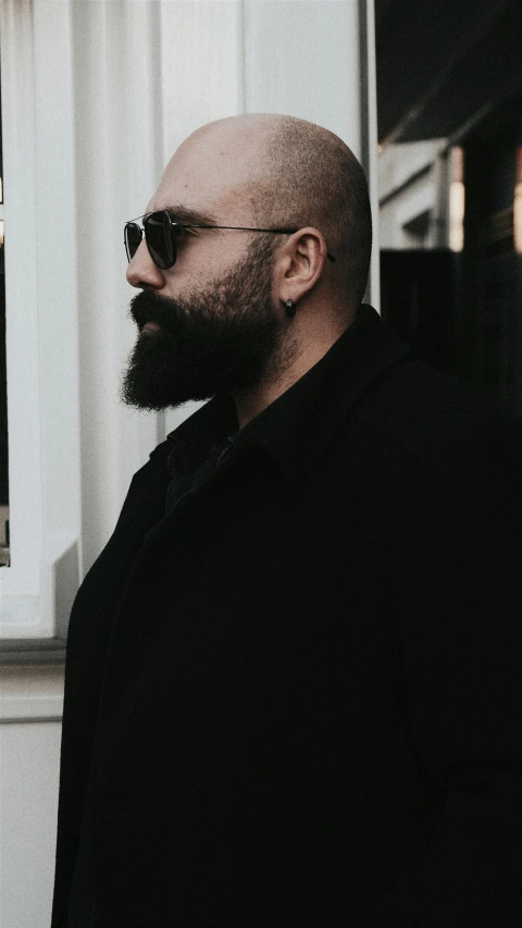 a bald man in sunglasses standing outside his apartment window