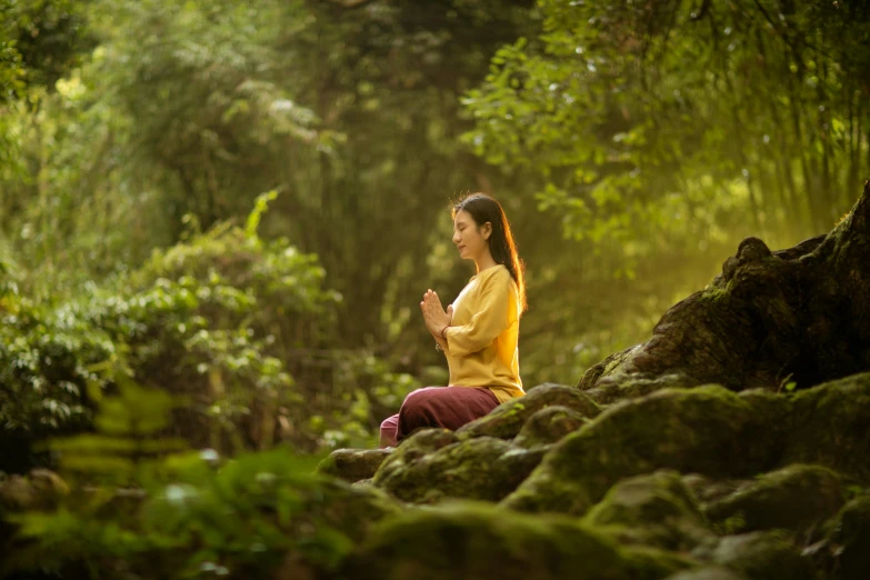 a girl in a yellow shirt sits in the woods