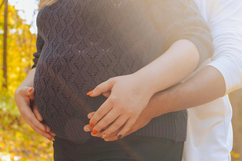 a pregnant woman holding her stomach outside in the fall
