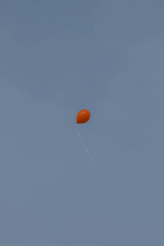 an orange balloon flies up into the blue sky