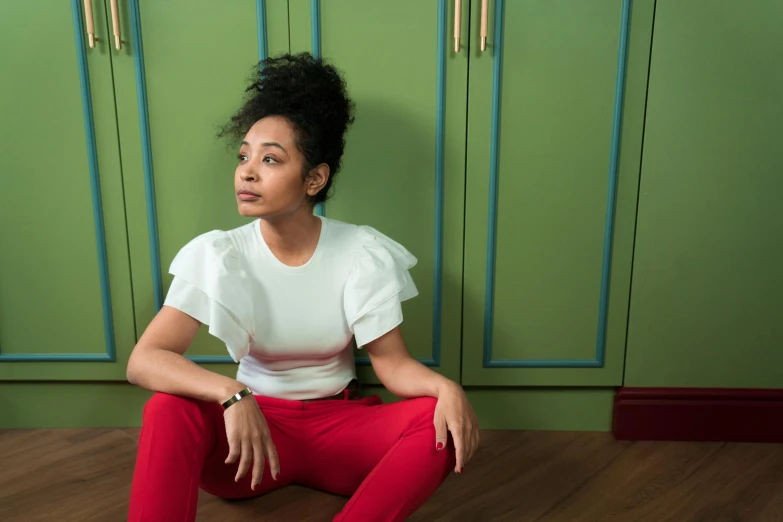 a young woman with her hair in an afro sits against a wall