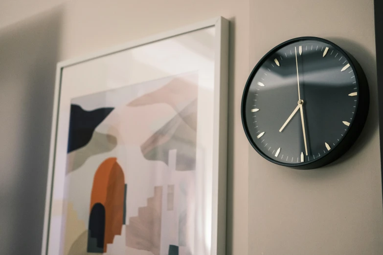 a clock is on the wall with a framed art in the background