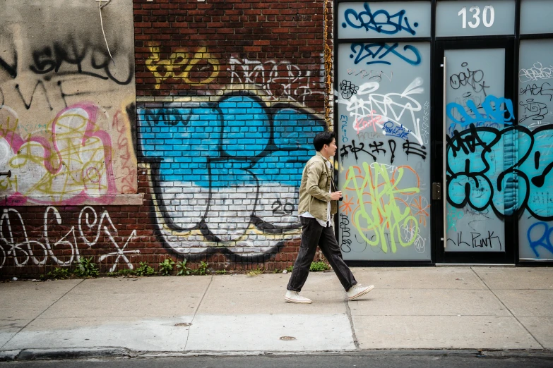 a man walking past a brick building covered in graffiti