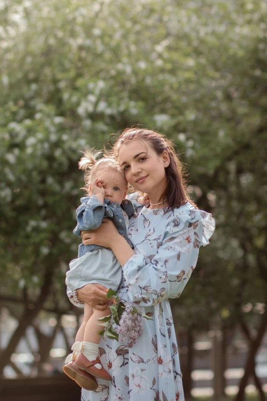 young woman holding baby next to flowers in bloom