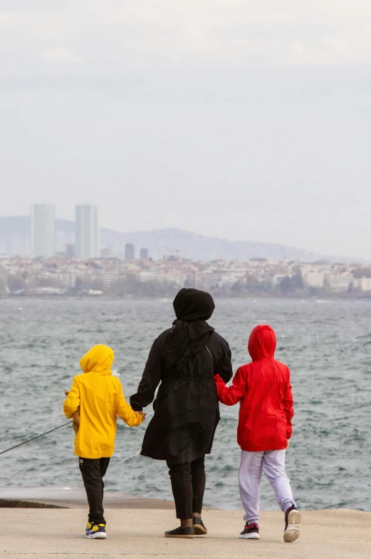 two women and one boy standing on a dock by the water with boats in the distance