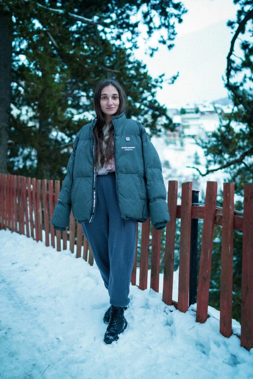 woman standing on snow covered hillside next to wooden fence