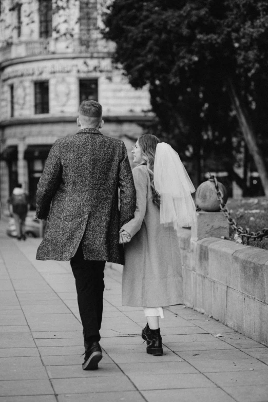 a bride and groom walking hand in hand down the sidewalk