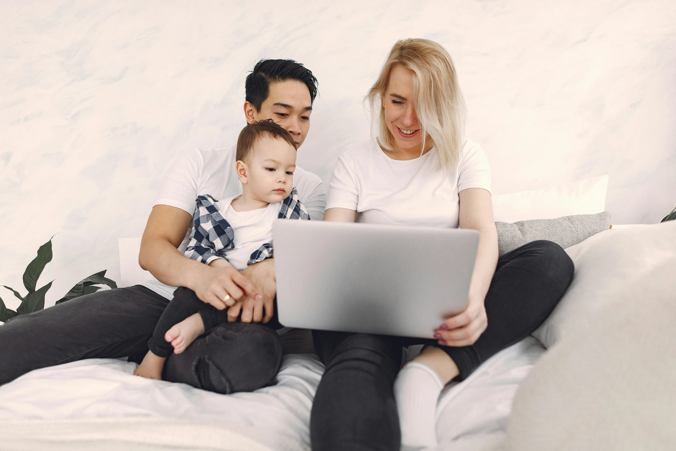 a couple sits with their son and a laptop on a bed