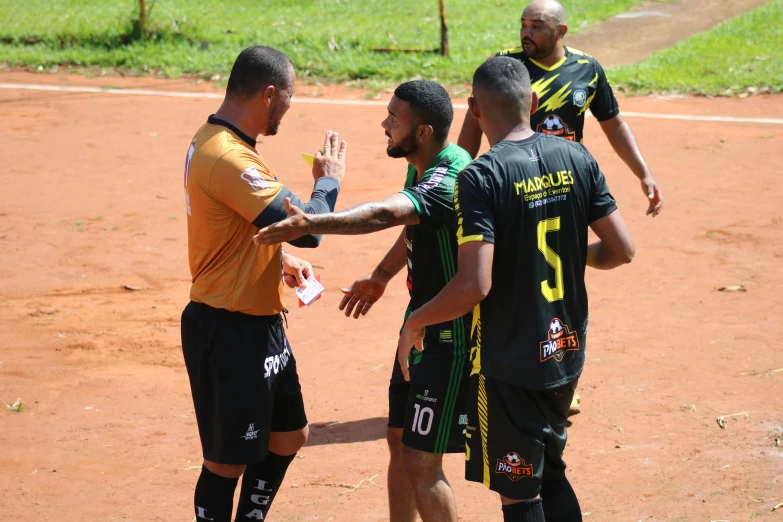 three men wearing soccer uniforms shake hands over an adult