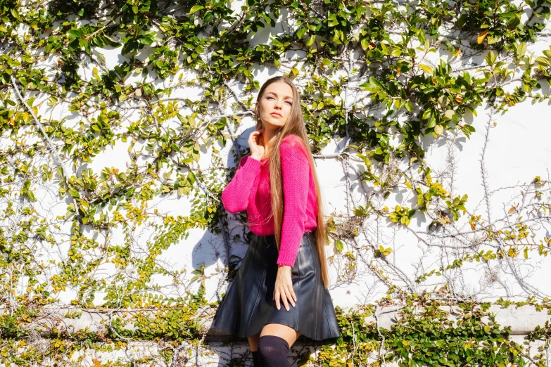 a woman in black stockings and a pink sweater is leaning against a wall