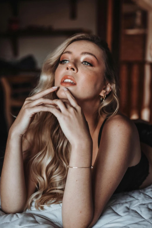 woman with blond hair, looking back with hand near mouth on bed