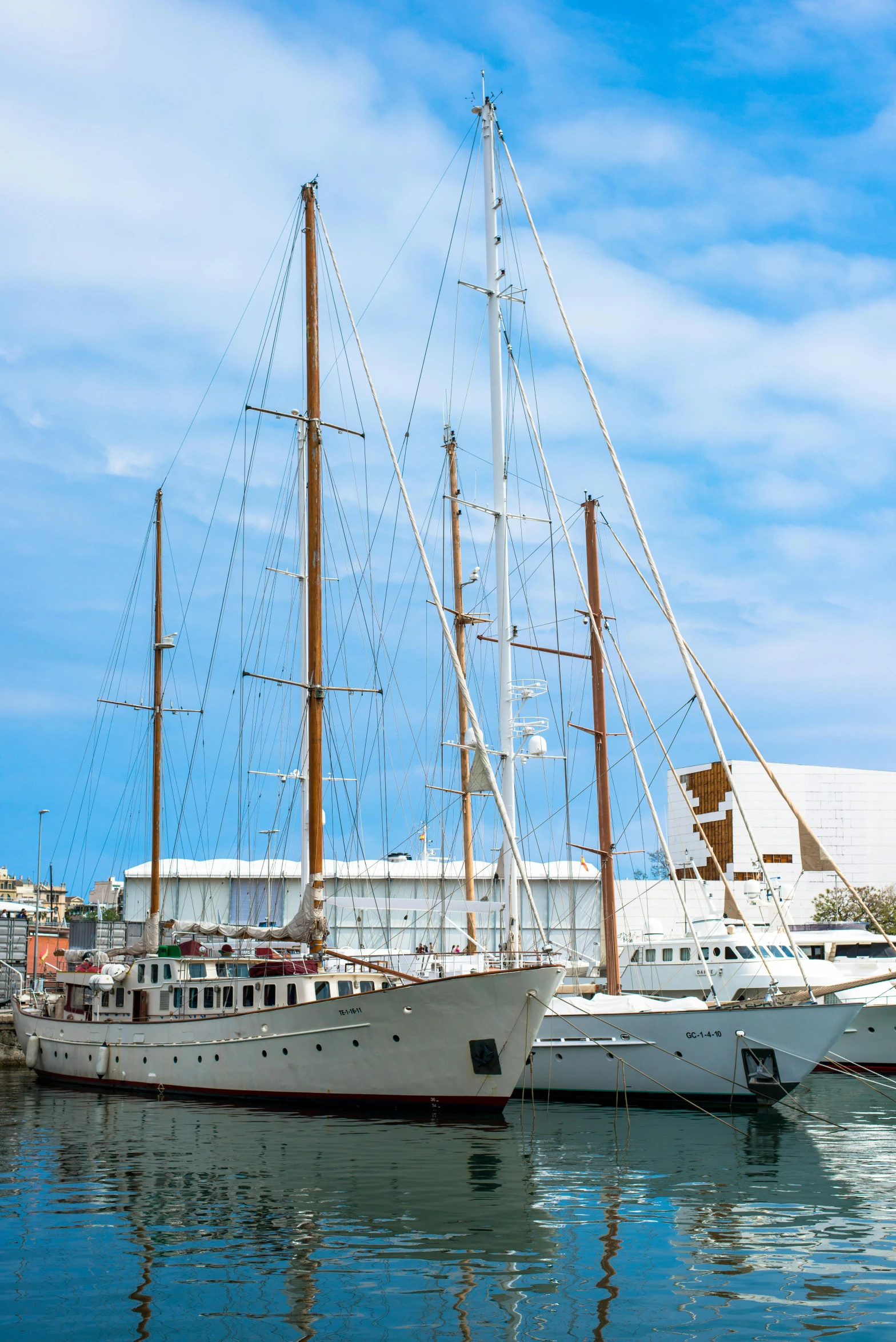 several large sail boats in the water by a dock