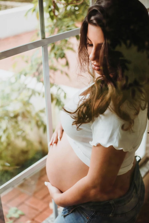 a pregnant woman in a white shirt sitting on a windowsill