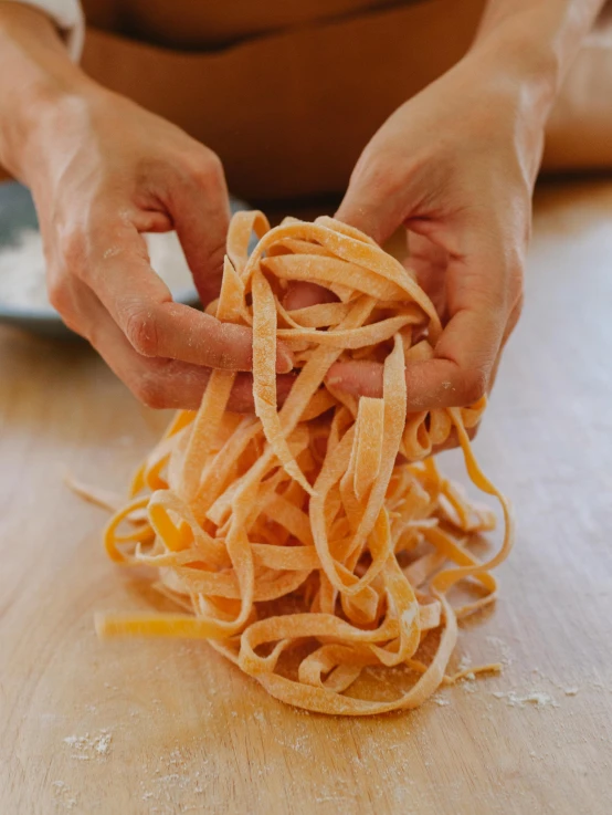 a person preparing a spaghetti dish with a hand holding the noodles