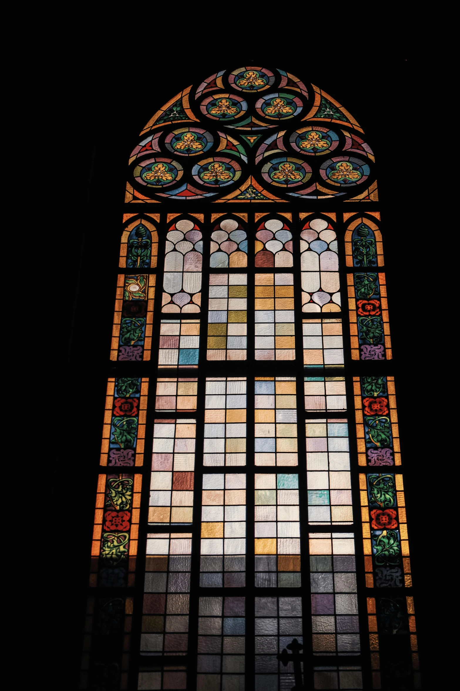 a large window in a dark building that has lots of stained glass