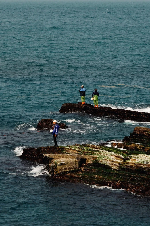 three people with umbrellas stand on the rocks near water