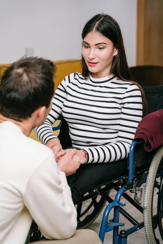 a woman with long black hair sits in a wheelchair and talks to an older man