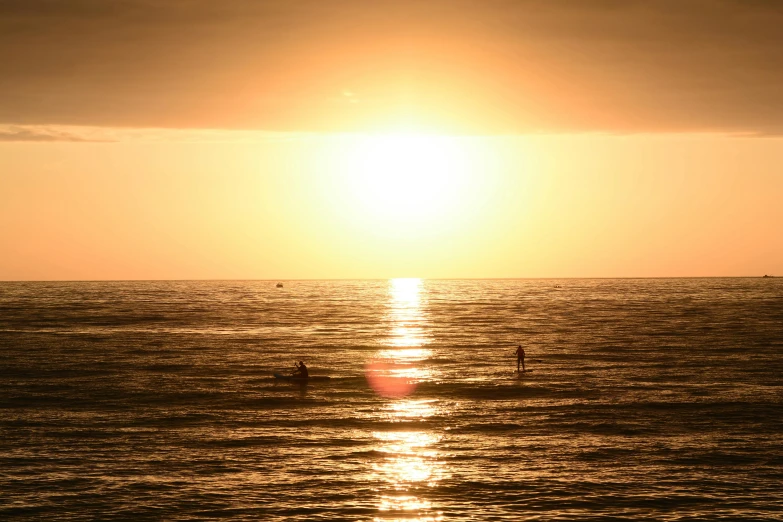 two people are out on their surf boards at sunset