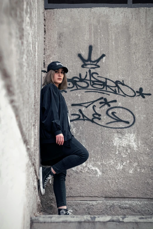 the woman is standing by a wall with graffiti on it