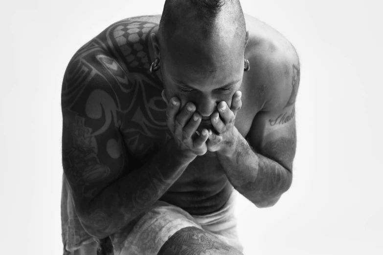 tattooed man sits cross legged on a stool