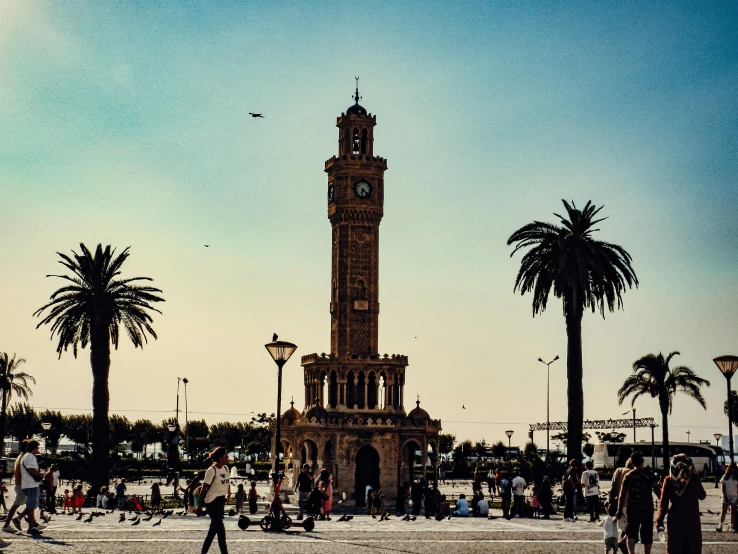 many people walking around a clock tower in the middle of town