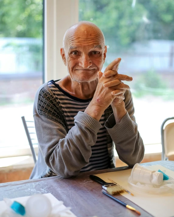 an older man sitting at a table making soing with his hand