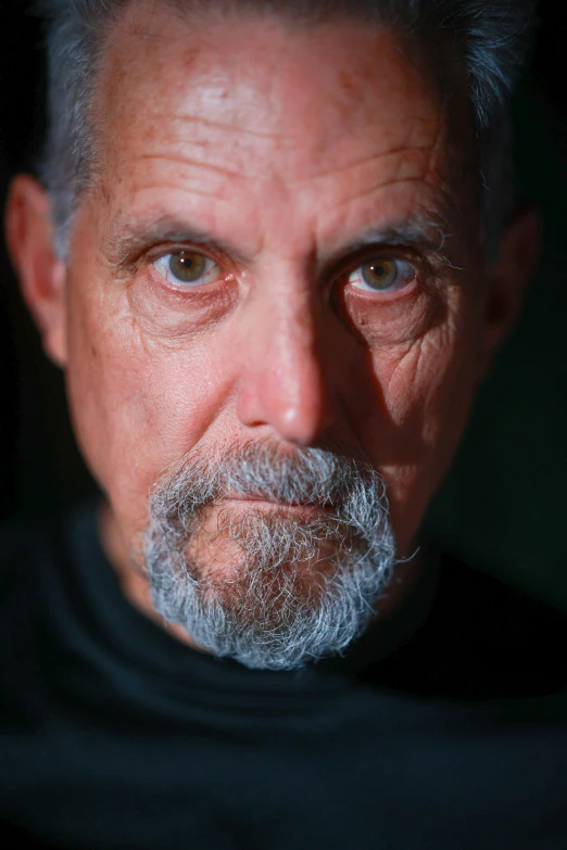 a close up of a man with grey hair and wearing a black shirt