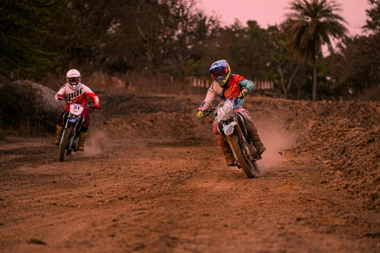two dirt bike racers are racing down a dirt track