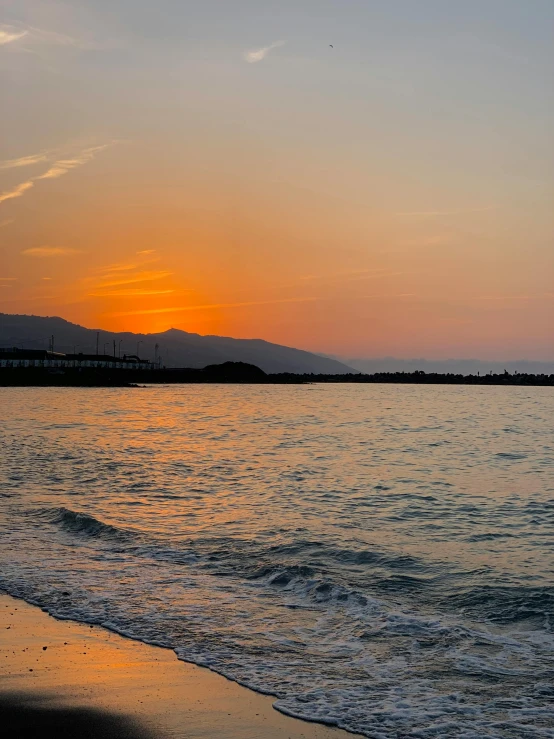 a sunset over the ocean with a pier in the distance