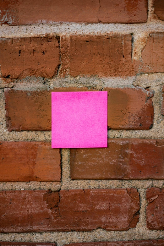 a pink post - it note sitting on top of a brick wall