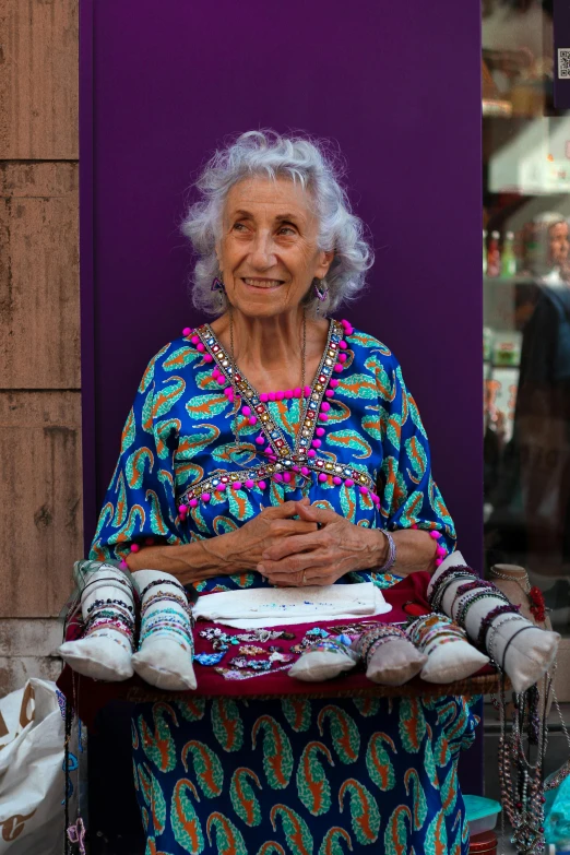 an older woman standing next to a wall, with her hands in her pockets