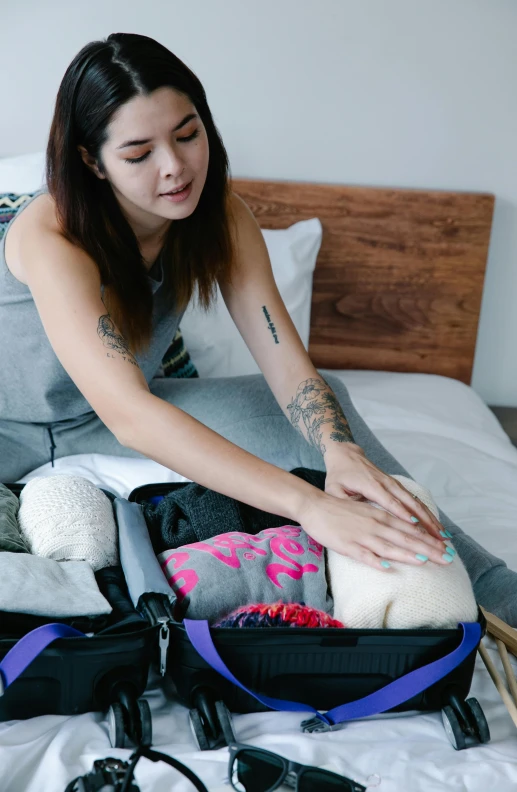 a woman is packing an open suitcase on the bed