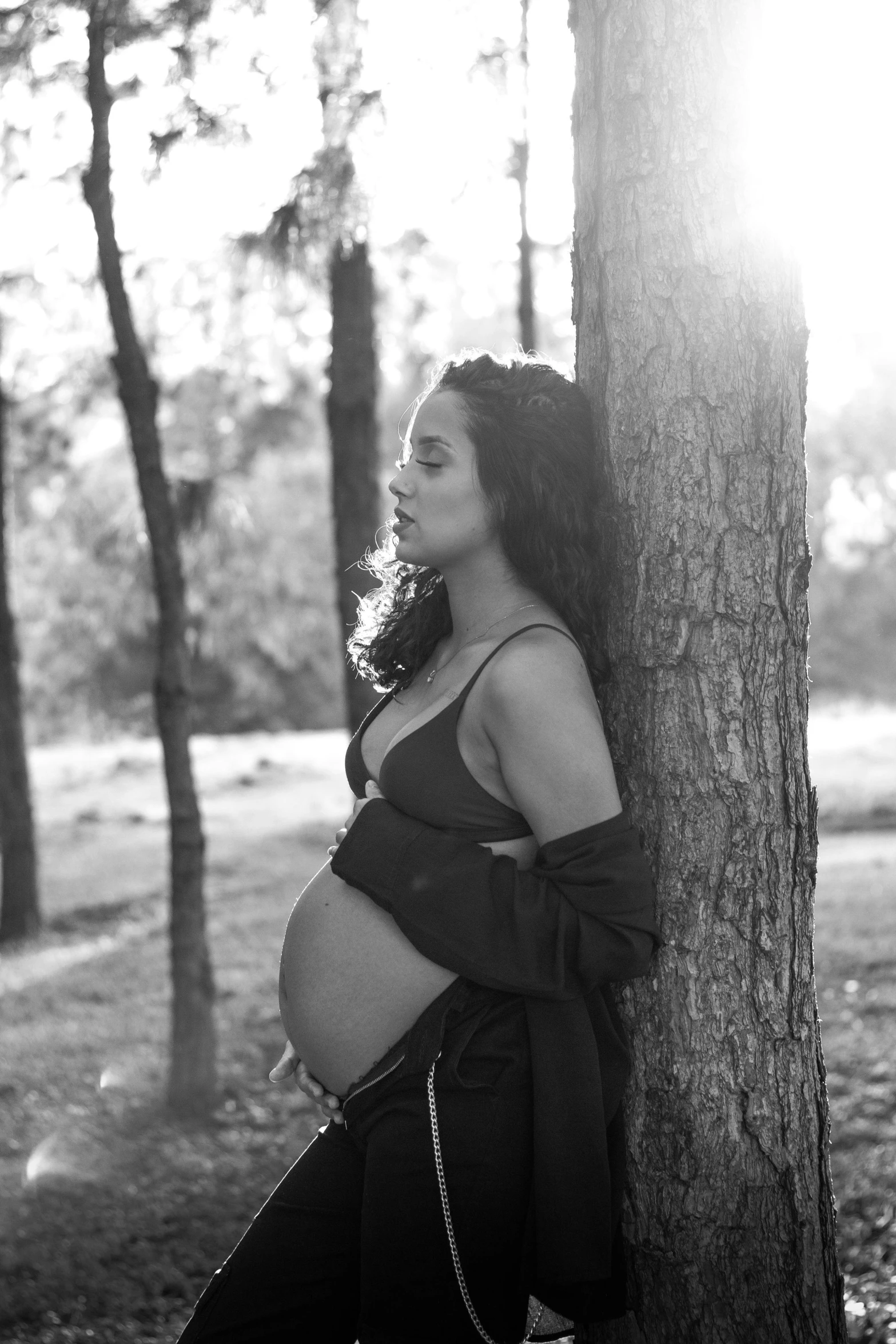 a pregnant woman wearing a bikini standing against a tree