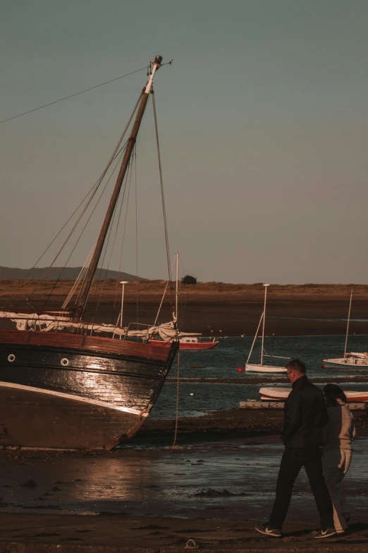 a couple walk along the shore towards boats