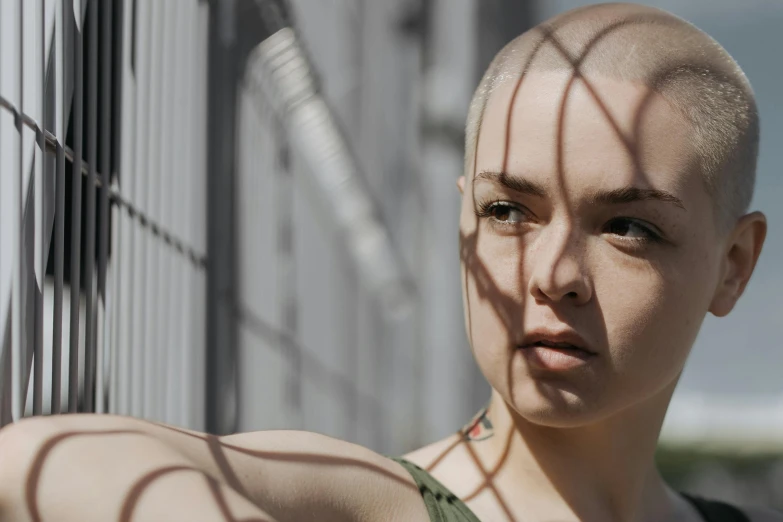 a young woman with a shaved head is seen behind a wire fence